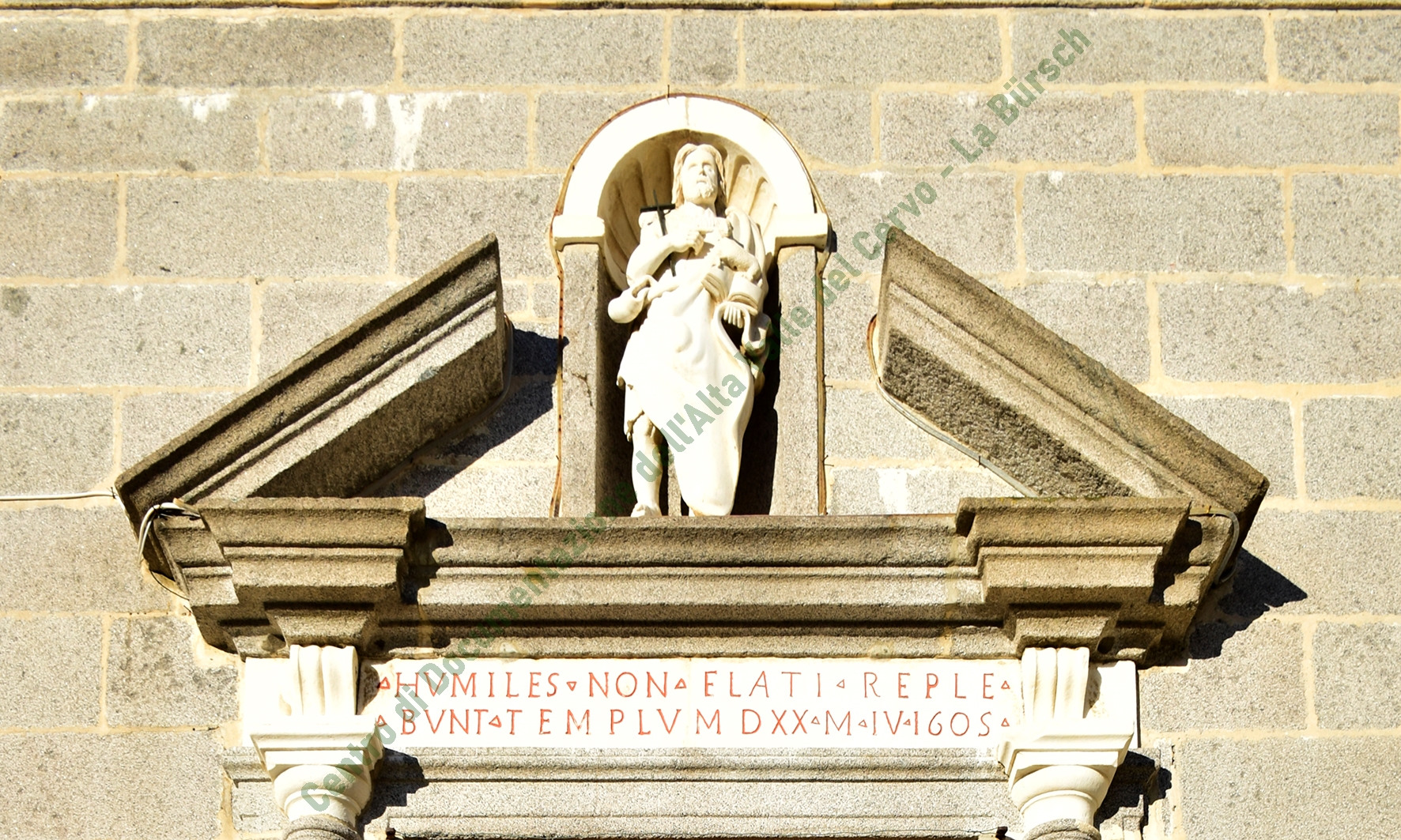 Il timpano spezzato che sormonta il portale della chiesa di San Giovanni d’Andorno: la statua del Battista e la facciata di pietra rappresentano l’esordio del Barocco nella Bürsch