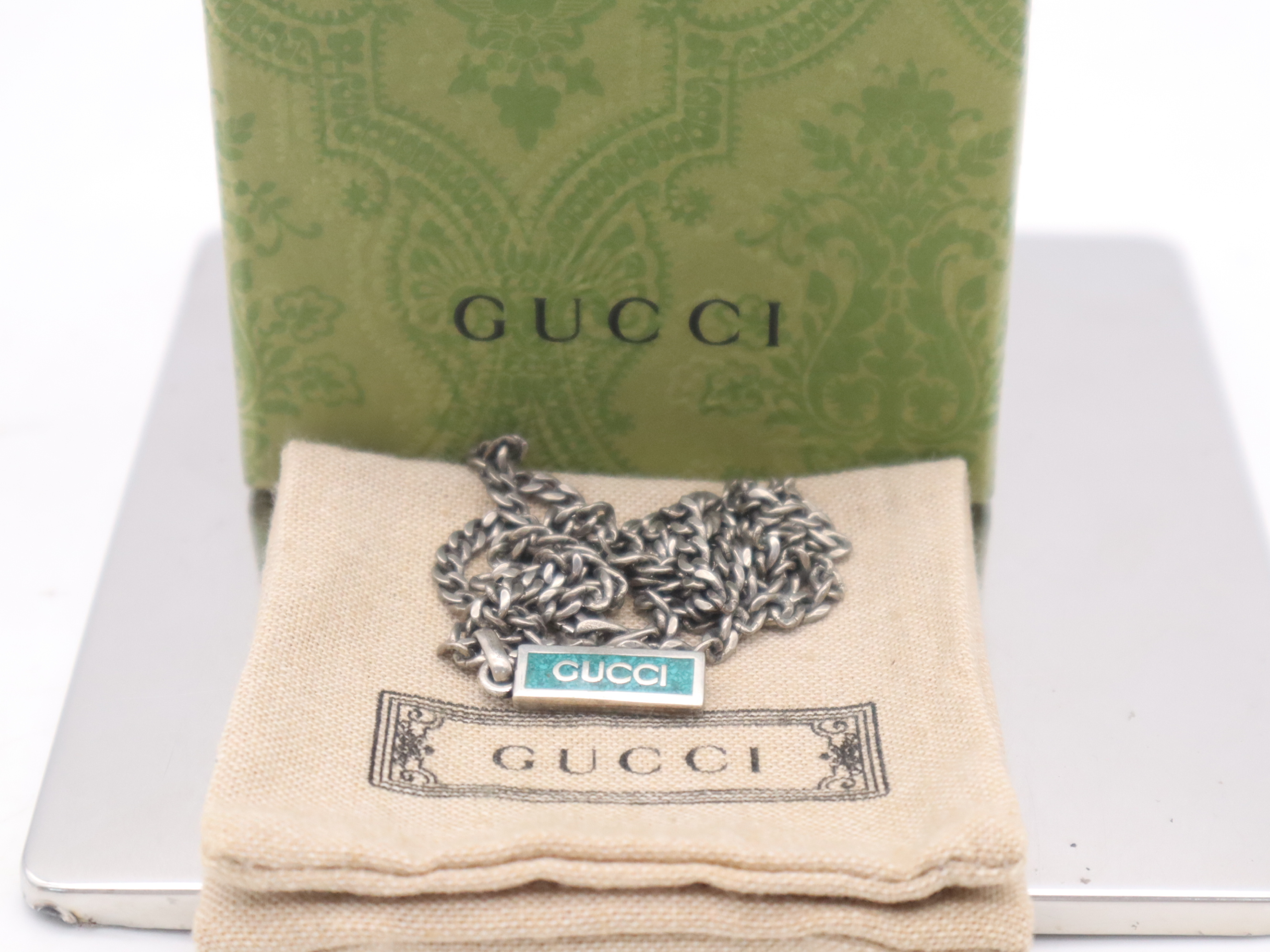 necklace with silver logo plate, box, and dust bag.