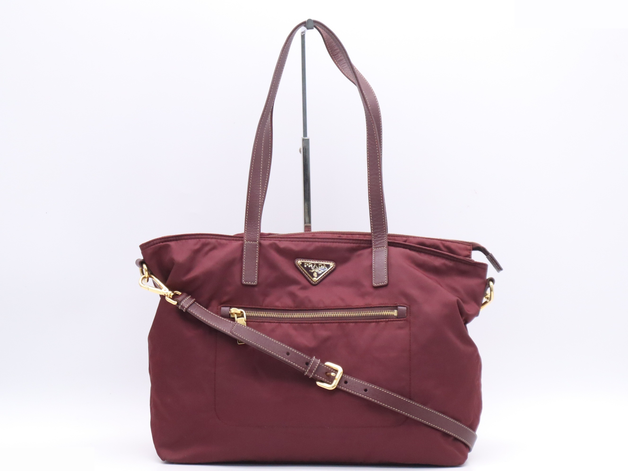 Nylon tote bag with triangular logo, red, gold hardware, and shoulder strap.