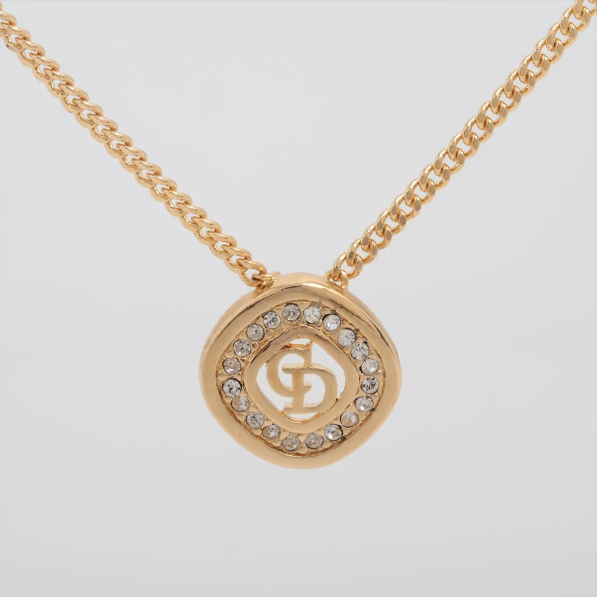 CD logo necklace, gold-plated with rhinestones. Shows wear, tarnishing, and stains.