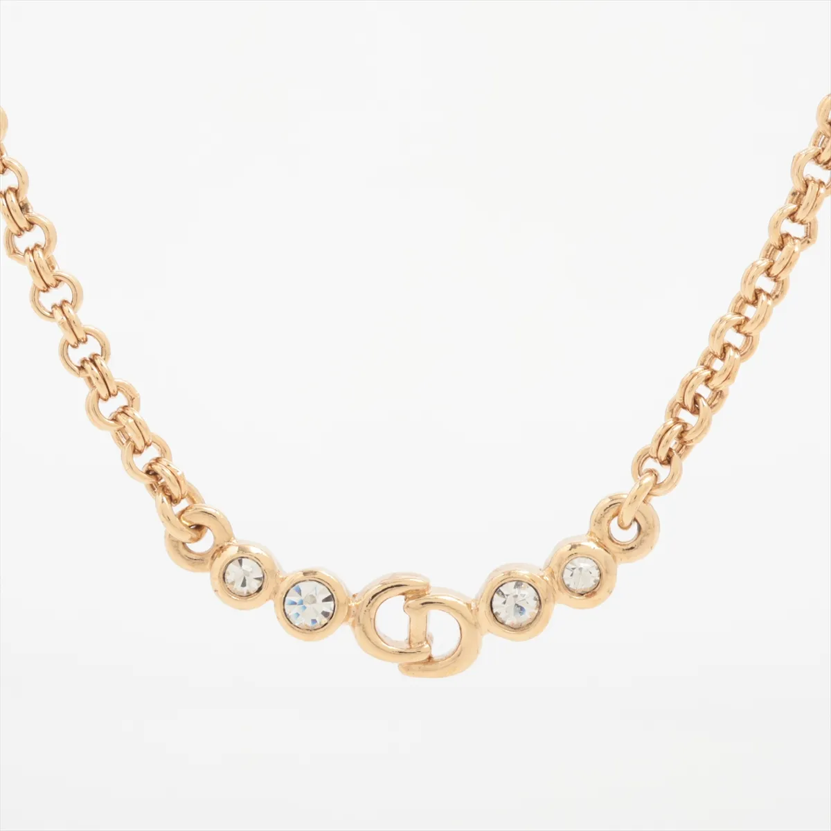 CD logo necklace, gold-plated with rhinestones. Shows wear, tarnishing, and discoloration.