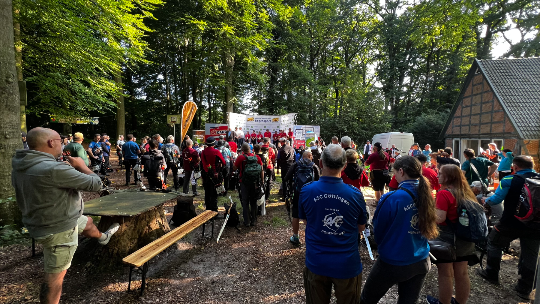 Bogenschützinnen und Bogenschützen stehen morgens bei einer Feldbogenmeisterschaft im Wald zusammen