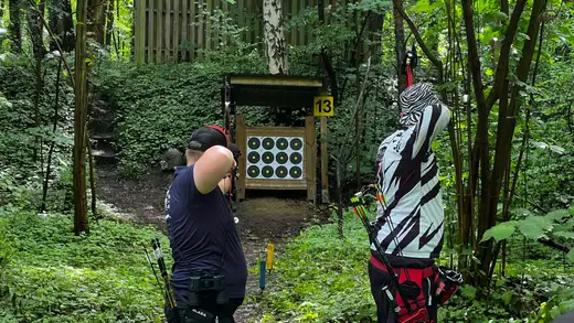 Zwei Schützen im Wald bereiten sich auf den Schuss auf eine Zielscheibe vor. Die Landesmeisterschaft Feldbogen 2026 in Wolfsburg.