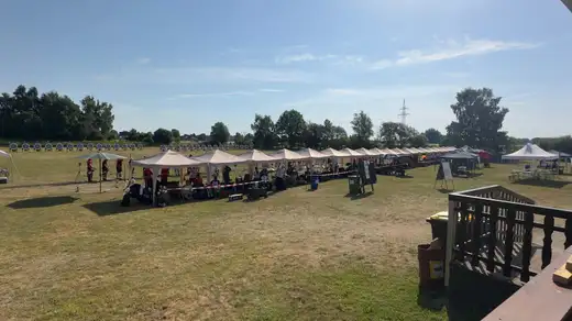 Teilnehmer der Landesmeisterschaft WA im Freien in Dannenberg unter Zelten, im Hintergrund die Schießlinie mit Zielscheiben.
