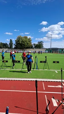 Schützen stehen auf dem grünen Wettkampffeld unter blauem Himmel an der Schießlinie.