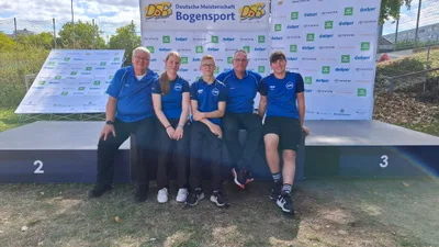 Fünf Mitglieder des ASC Göttingen sitzen vor der Siegerehrungswand der Deutschen Meisterschaft Bogensport 2026 in Wiesbaden.