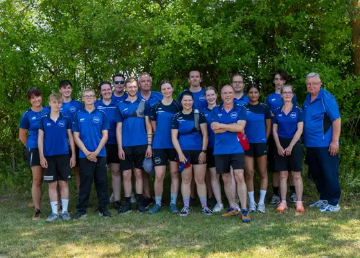 Gruppe von Bogensportlern des ASC Göttingen in blauen Vereins-Trikots vor Bäumen.