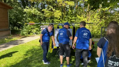 Mitglieder in blauen ASC-Shirts stehen am Heck des geschmückten Kleintransporters; ein großer Pfeil liegt auf dem Dach.