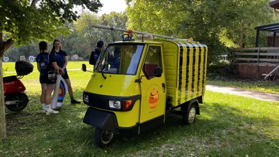 Gelber Kleintransporter mit schwarz-gelber Dekoration und großem Pfeil auf dem Dach vor dem Bogengelände.