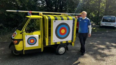 Ein Vereinsmitglied steht neben dem gelben Kleintransporter, dessen Seite eine große Zielscheibe schmückt.