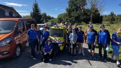 Mitglieder in blauen Vereinsshirts stehen mit dem geschmückten Wagen am Straßenrand.