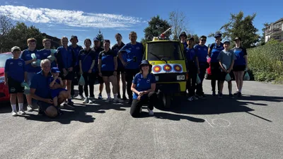 Kinder, Jugendliche und Erwachsene in blauen Vereinsshirts posieren rund um den gelben Kleintransporter mit Zielscheiben.