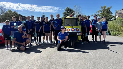 Unsere Gruppe steht bei Sonnenschein um den gelben Festwagen mit Zielscheiben und großem Pfeil auf dem Dach.