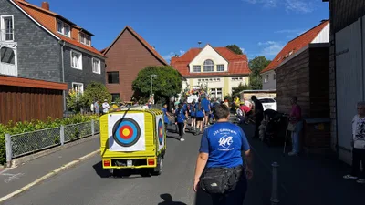 Blick auf den gelben Wagen mit Zielscheibe am Heck und die begleitende Gruppe in einer Straße mit Fachwerkhäusern.