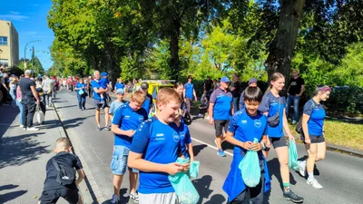 Junge Teilnehmer in blauen Vereinsshirts gehen mit Beuteln durch die Straße, dahinter folgen weitere Mitglieder.