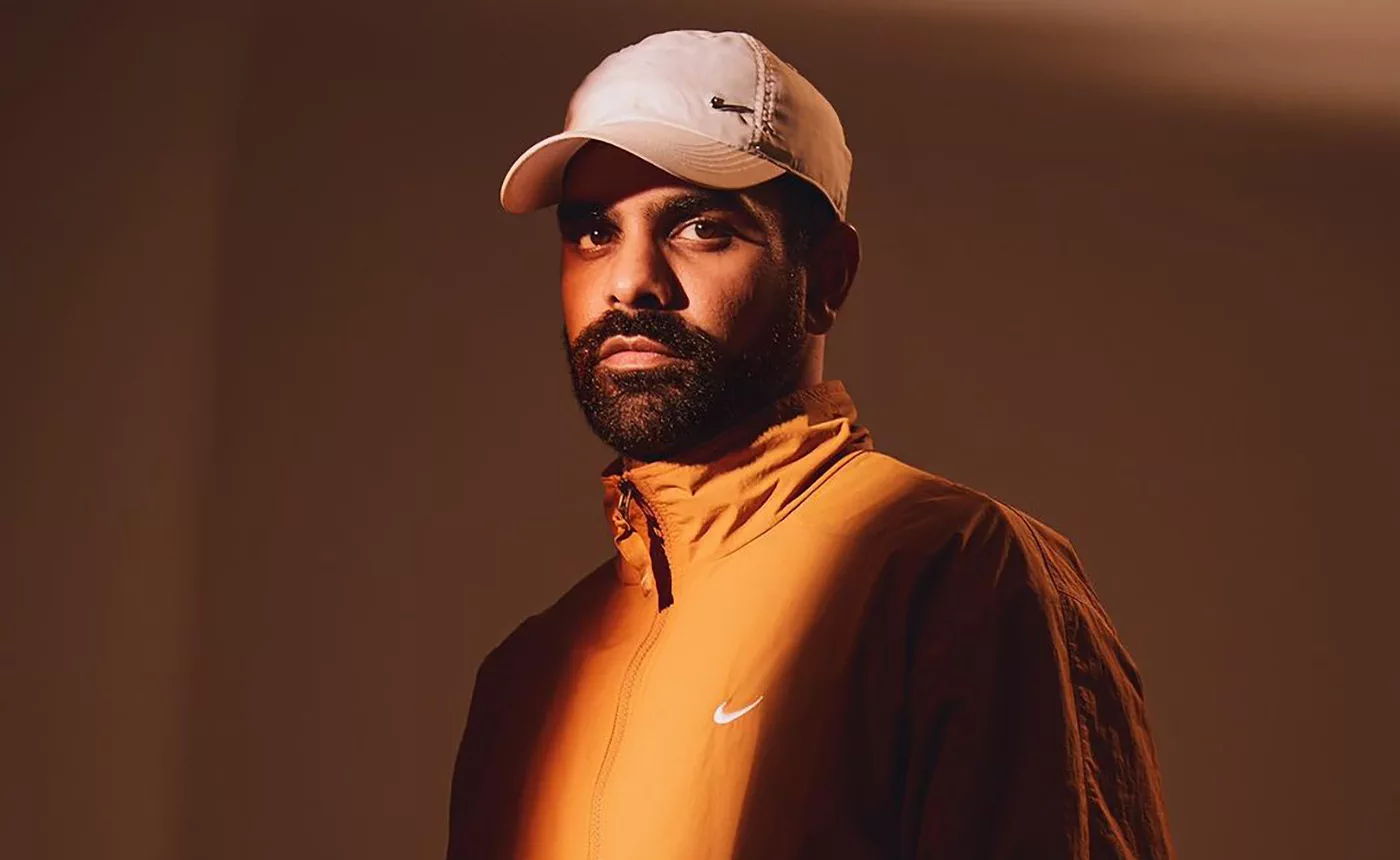Ahadadream in an orange jacket and cap in a studio-style promotional portrait