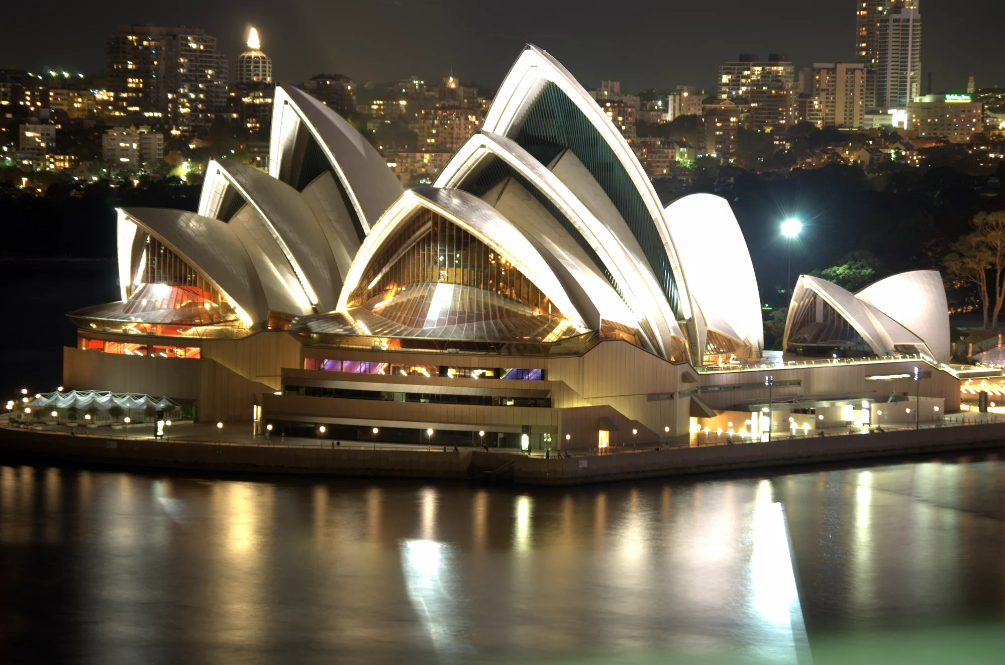 Sydney Opera House illuminated at night beside Sydney Harbour