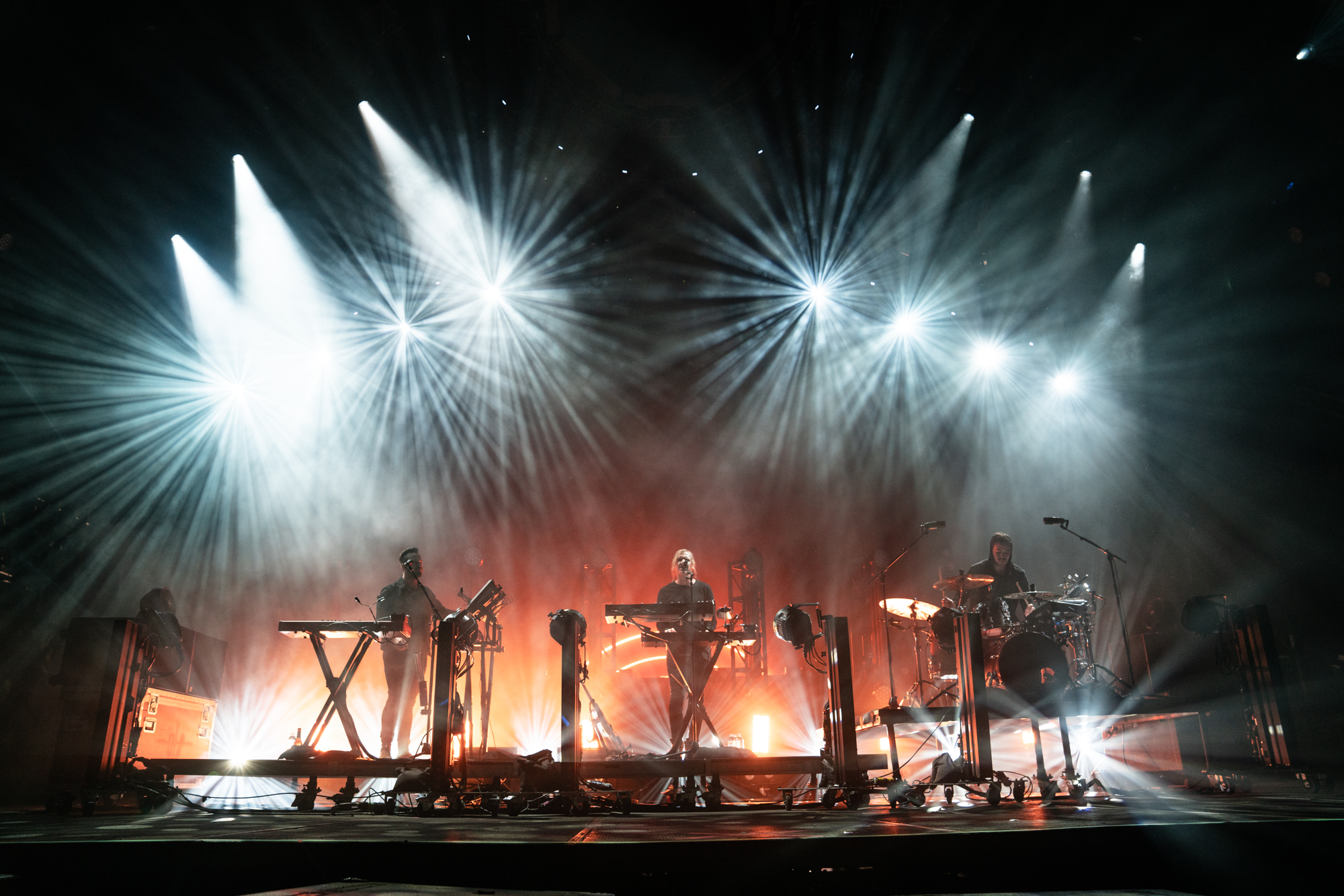 RÜFÜS DU SOL spielen als Trio auf einer von weißen Lichtstrahlen beleuchteten Bühne.