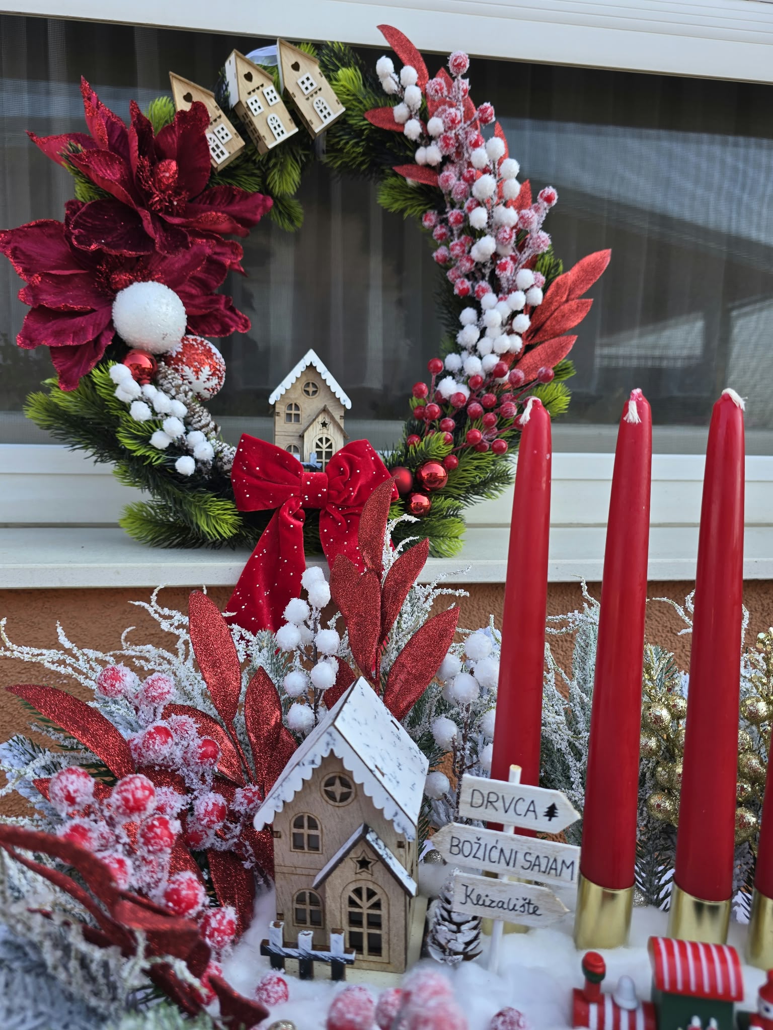 Red Christmas door wreath with a velvet bow and wooden houses