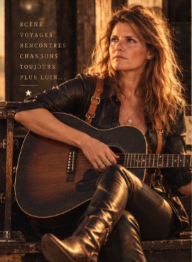 Cinematic wide portrait of a French female folk-rock singer-songwriter standing on a dusty desert road at dusk, acoustic guitar hanging on her back, worn leathe