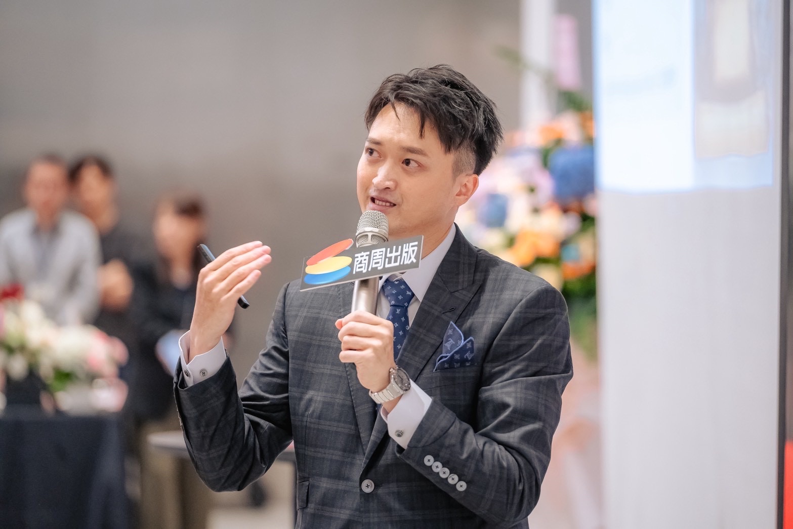 Editorial portrait of an Asian man in his forties wearing a dark navy suit and open collar shirt, seated, calm confident gaze slightly off camera, soft directio