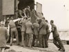 Men of the 84th (LT) AA (Anti-Aircraft) Regiment, TA (Territorial Army) unloading a piece of equipment from the back of a lorry at the regiment's training camp at Bude, Cornwall; the man on the left appears to be at least partly dressed in civilian clothing. A boy in short trousers, extreme foreground left, is watching the operation.