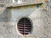 Extractor fan outlet with a heavy armoured grill and a gutter over the top.