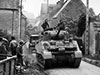 Sherman tanks driving through a small French village.