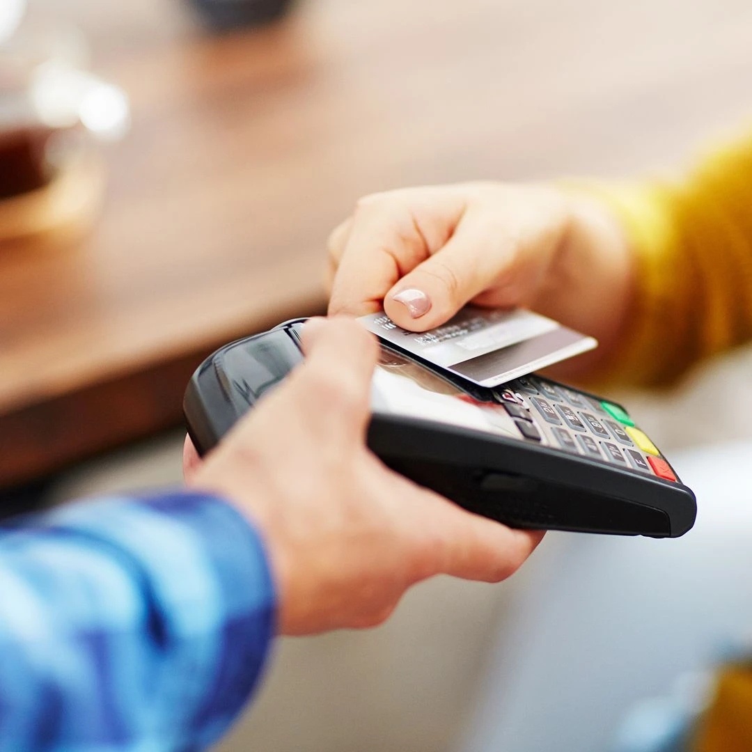 A man holds a credit card reader machine out to a woman who is tapping her credit card on the machine to pay.