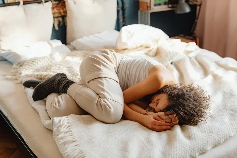 Person curled up in a ball, lying on a bed in a soft lit room