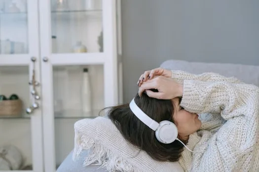 Woman lying on couch with headphones & hands on head