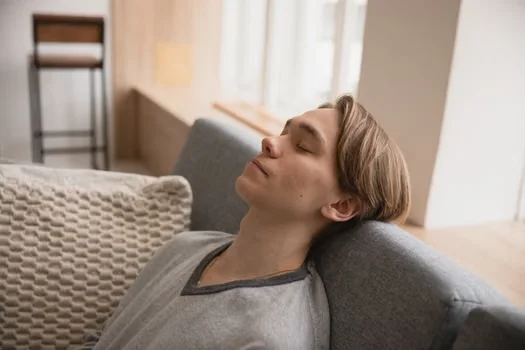 Young man exhausted, resting with his head back against the sofa