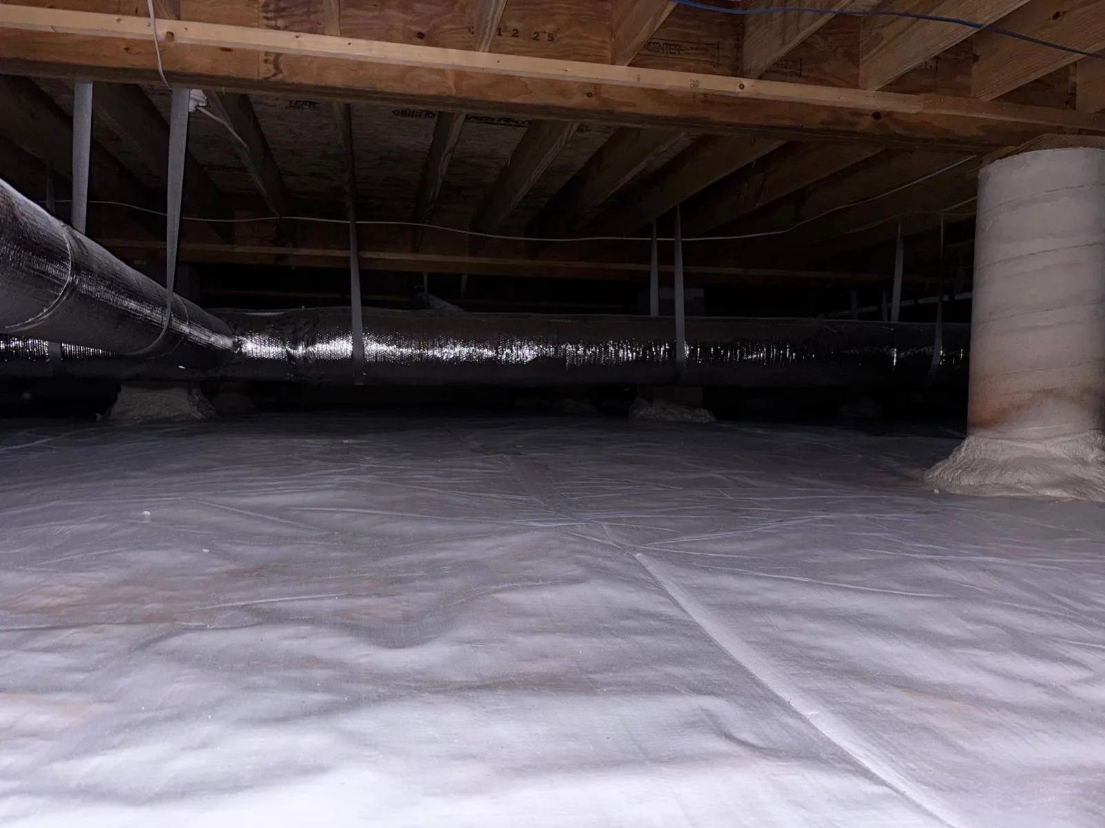 Crawl space with a white vapor barrier covering the ground and ductwork above