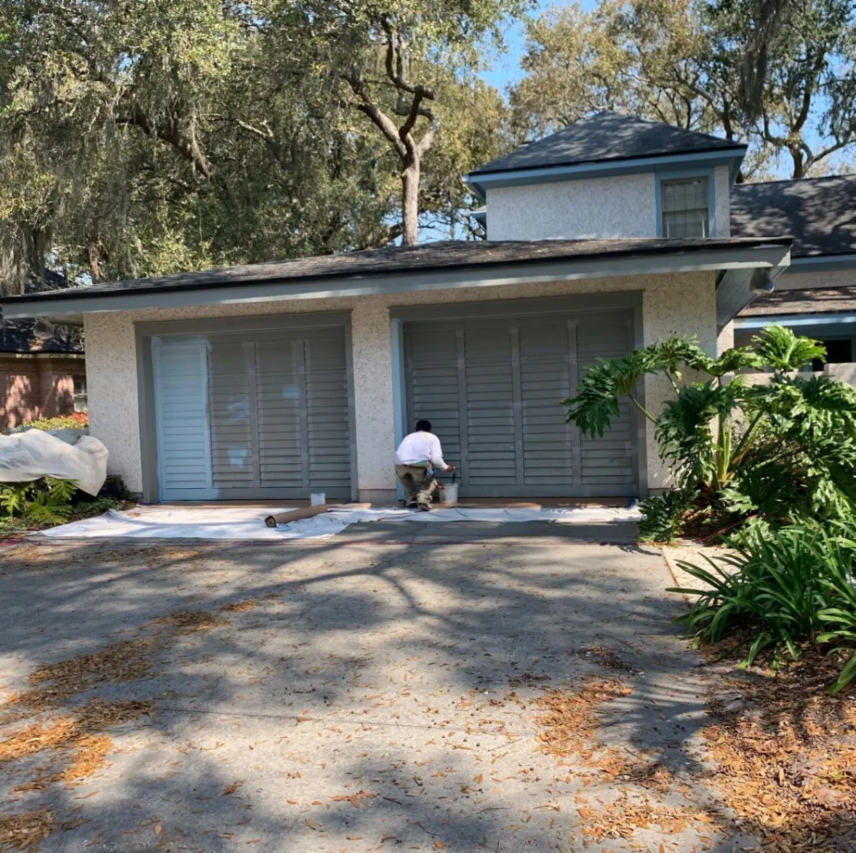 Painter working on the exterior of a garage beside a driveway