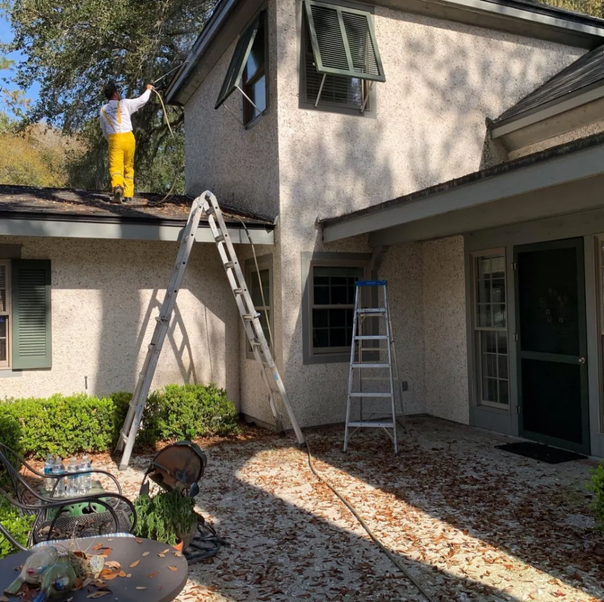 Painter on a ladder repainting the stucco exterior of a two-story home