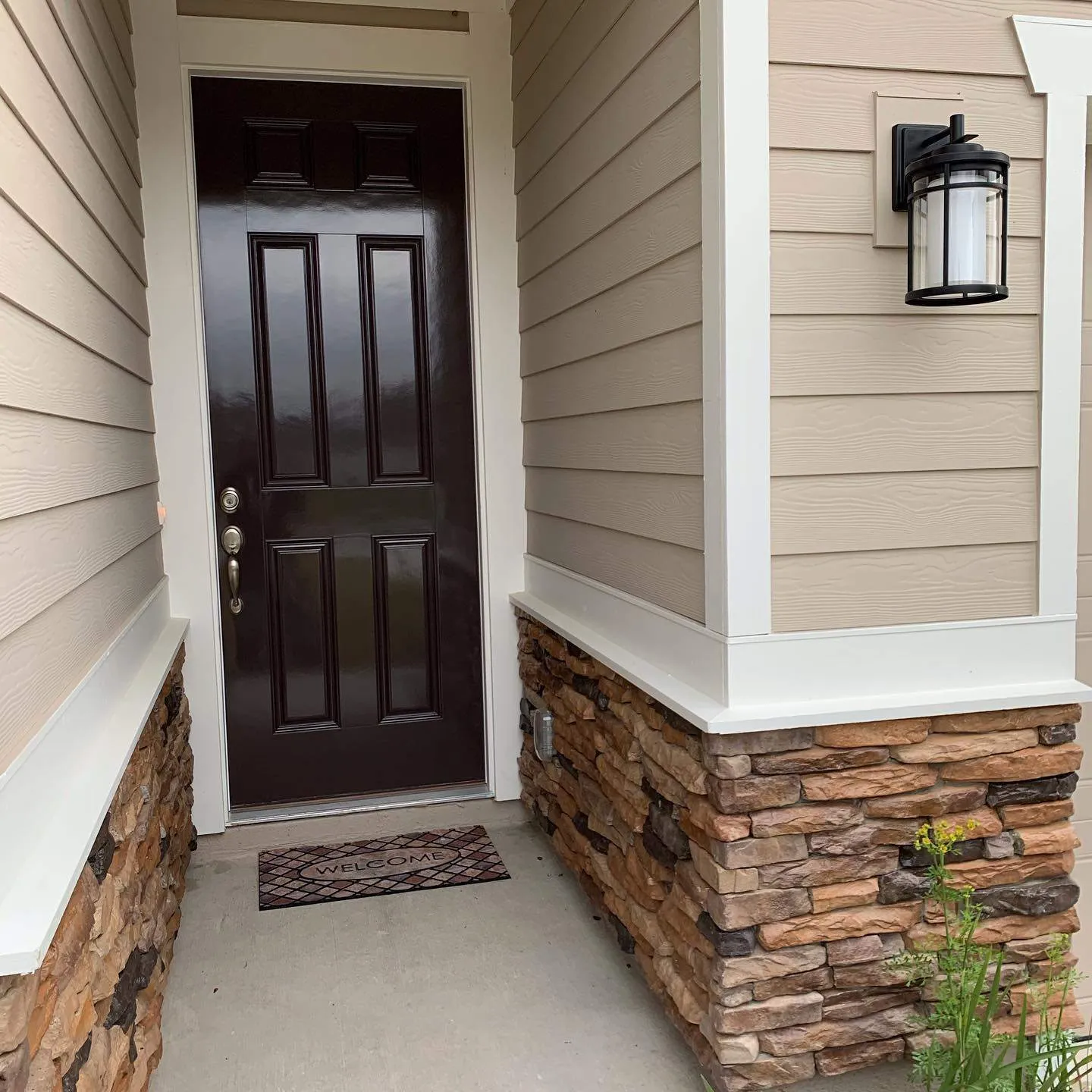 Front entry of a newer home with tan siding, white trim and a freshly painted dark door