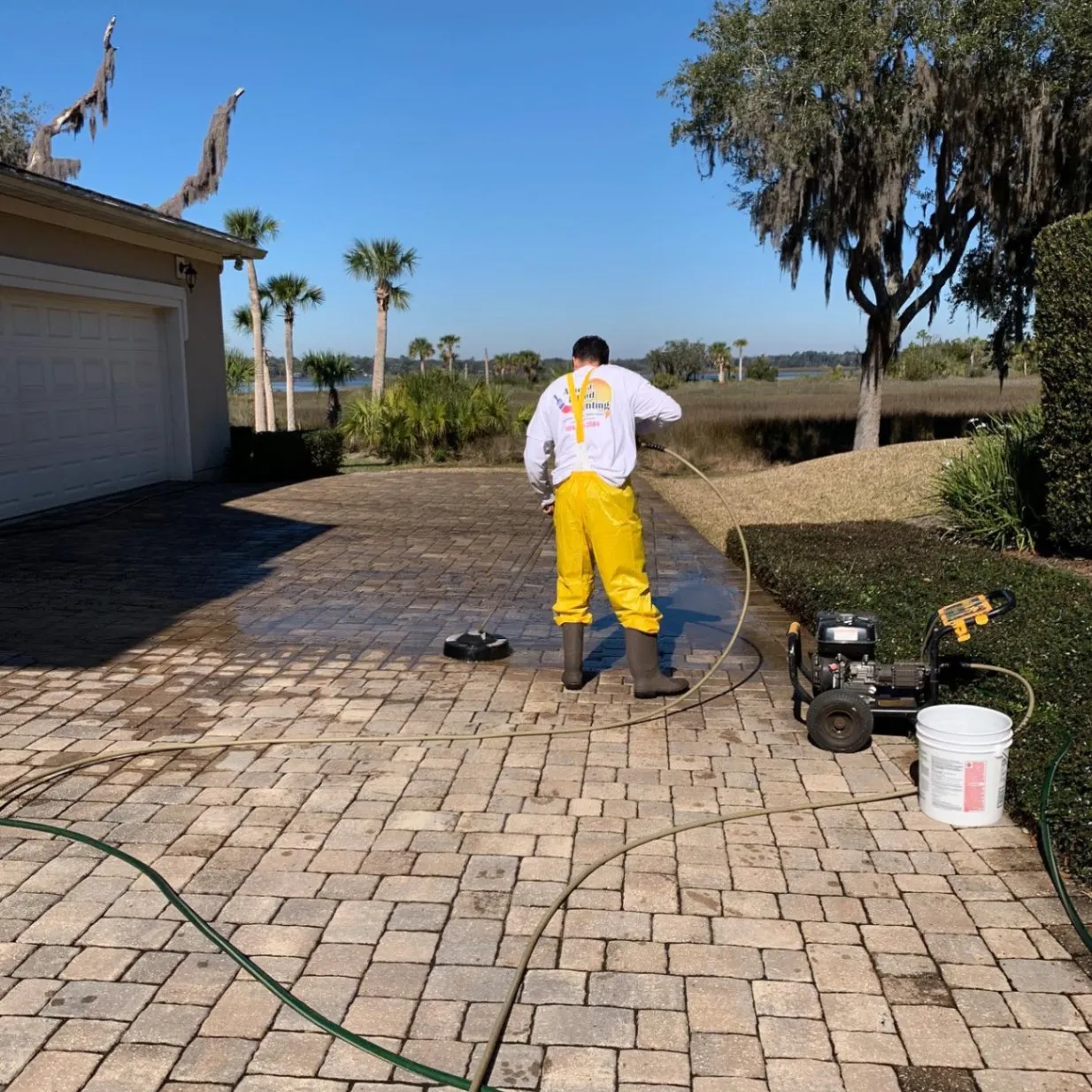 Technician pressure washing a paver driveway next to a home
