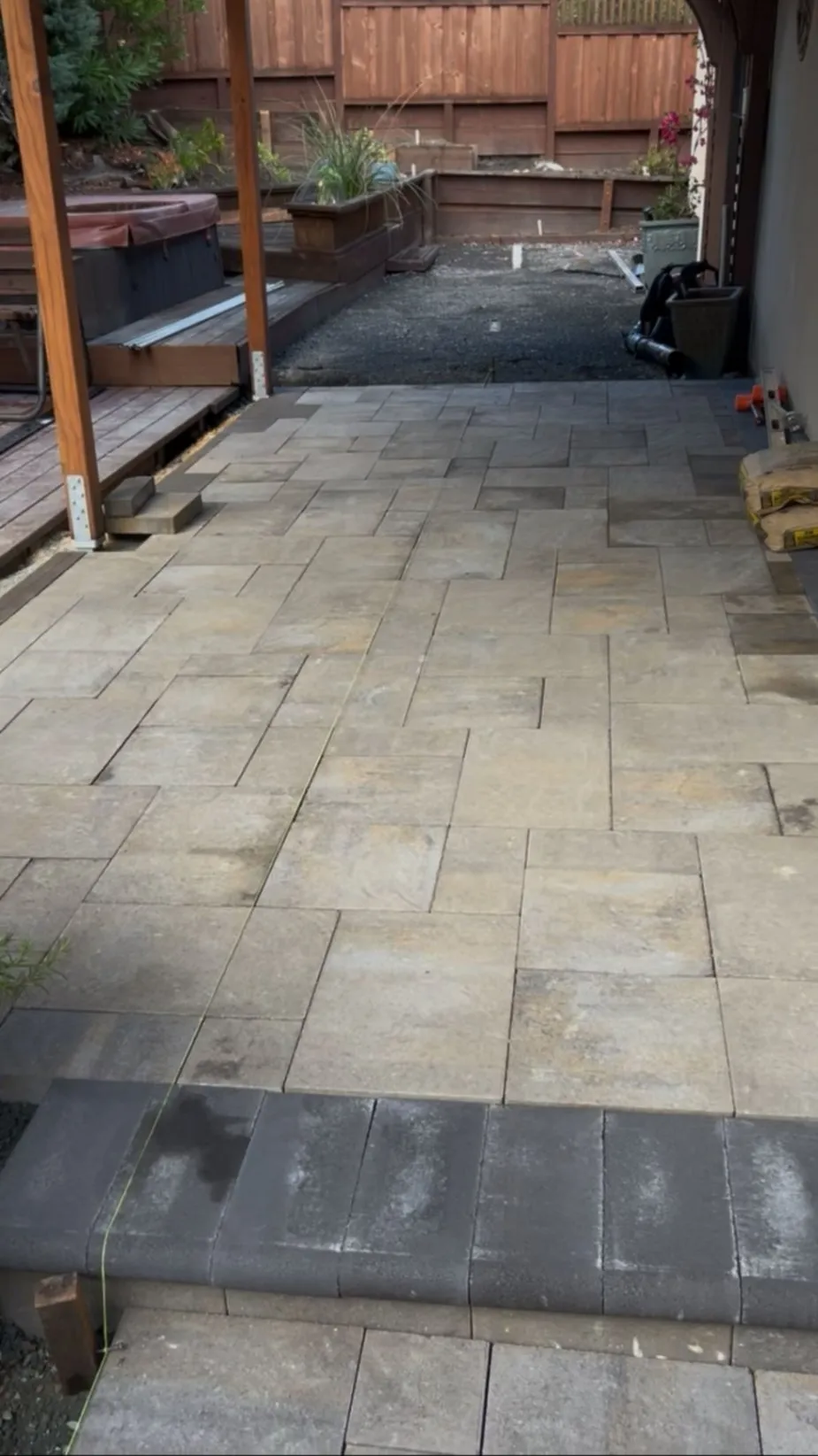 Large-format paver side-yard patio next to a wood fence and planter beds