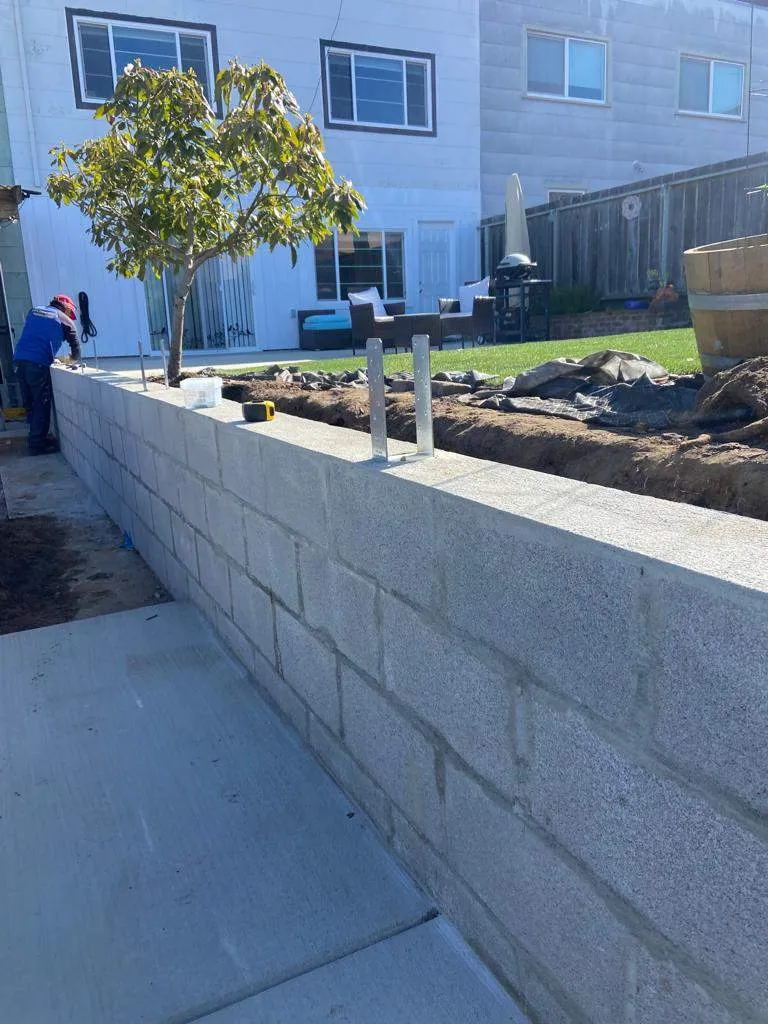 Gray concrete block retaining wall along a concrete walkway with a planted terrace above