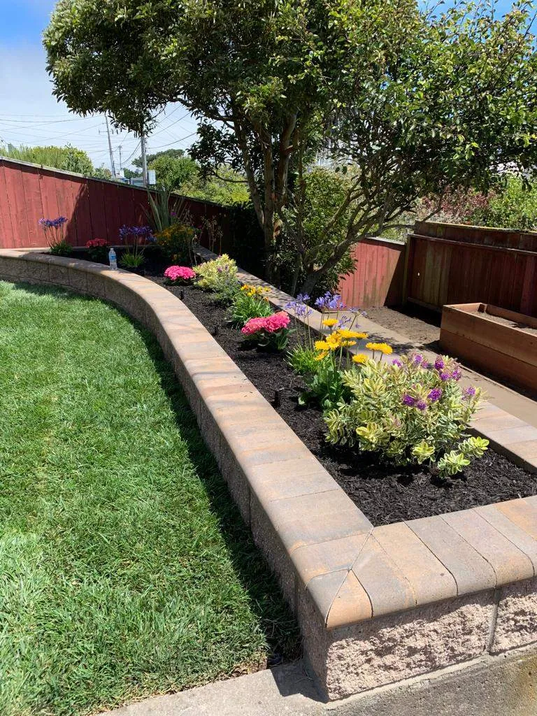 Low curved block planter wall with flowering plants beside a green lawn