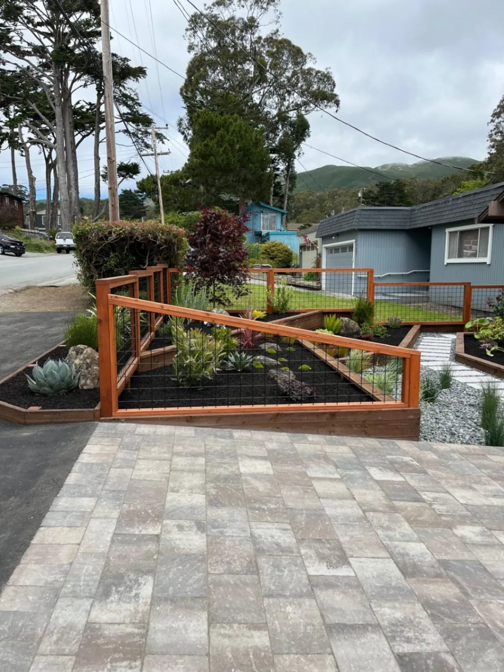 Front-yard paver driveway lined with redwood-framed planting beds