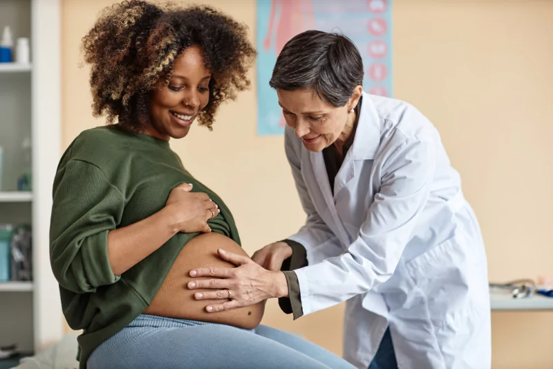 Doctor performing a routine checkup on an expectant mother, gently inspecting her belly in a clinic setting.