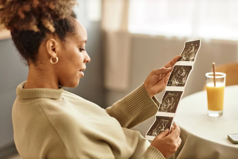 Mother viewing ultrasound images while sitting with a drink, illustrating moments of gratitude and bonding during Thanksgiving for pregnant moms.