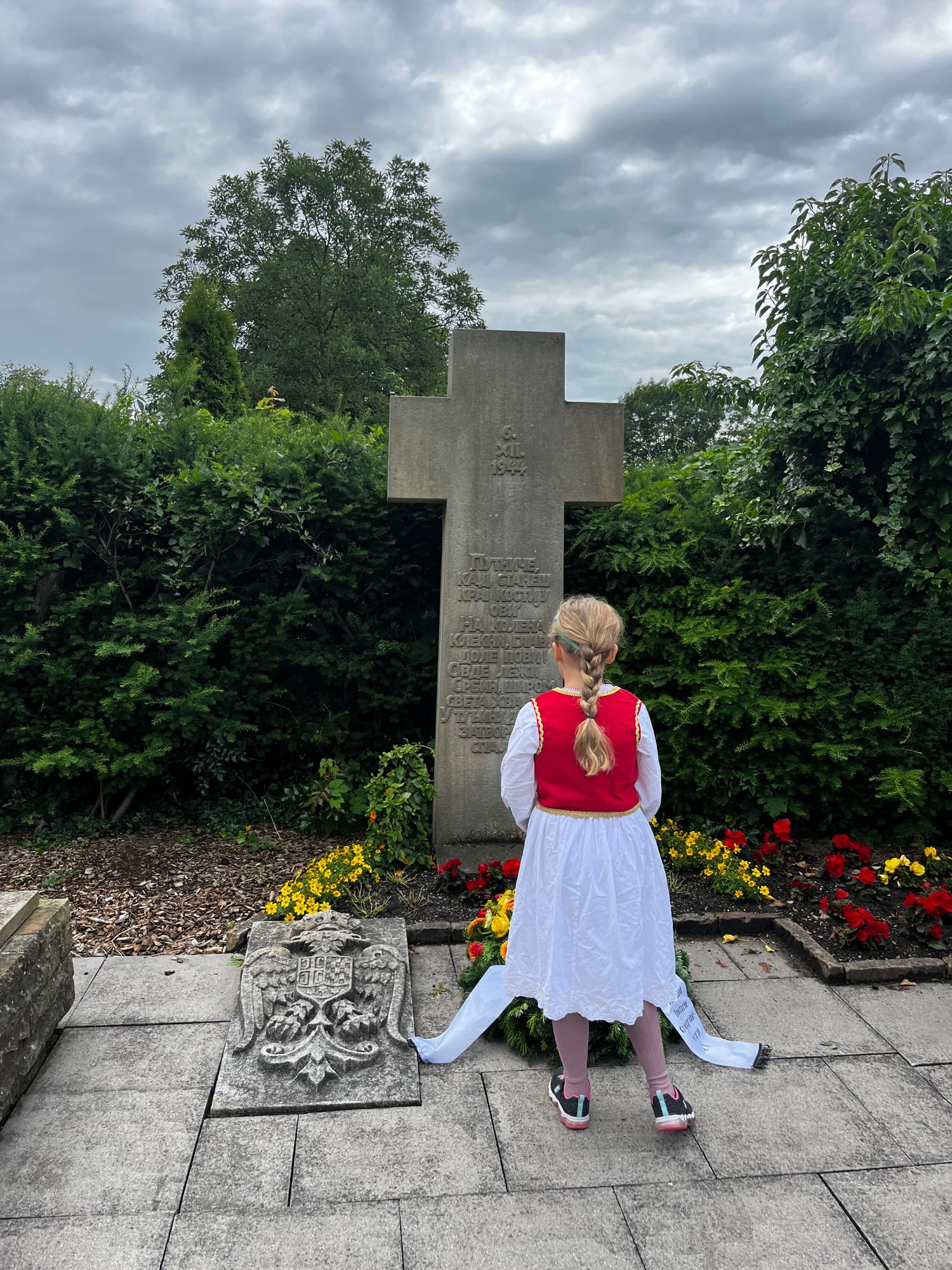 A young participant in folk costume pays her respects at the memorial cross