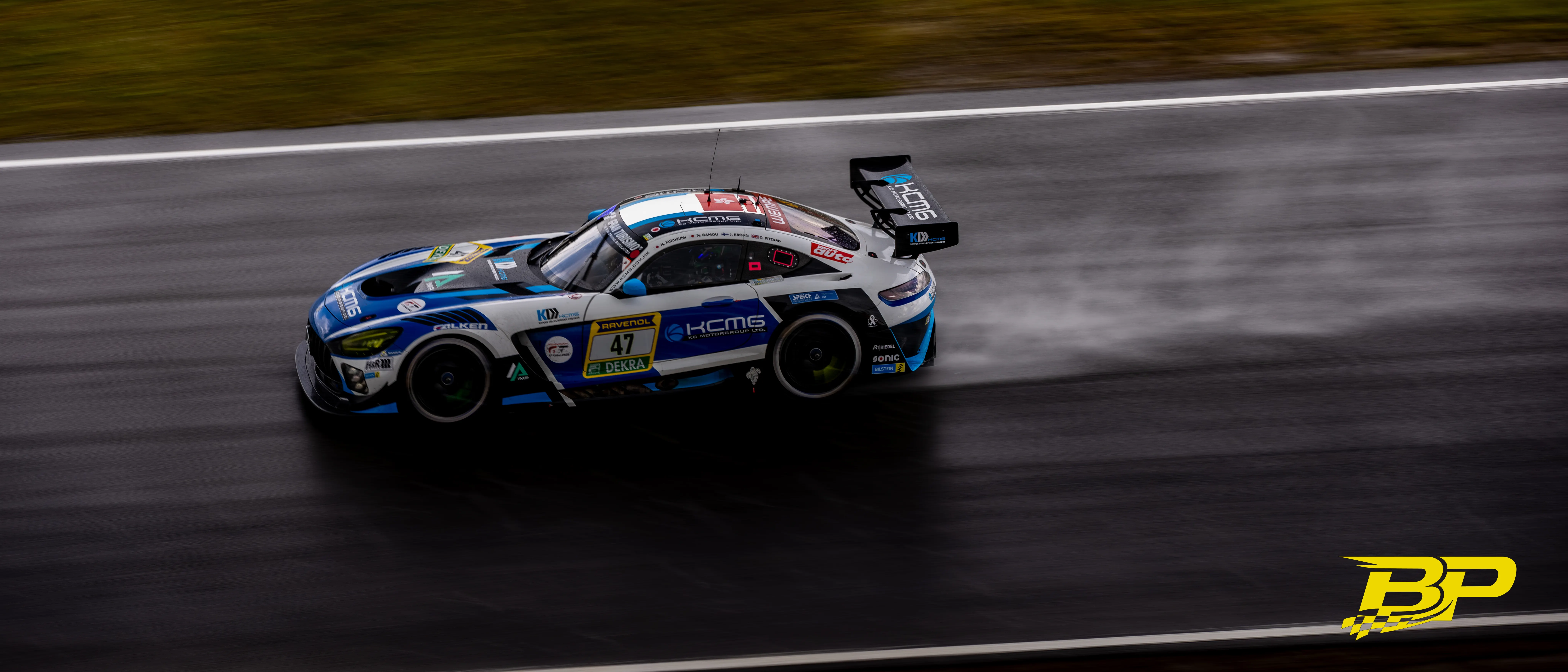 Blau-weißer GT-Rennwagen mit Startnummer 47 wirbelt auf der nassen Strecke Gischt auf.