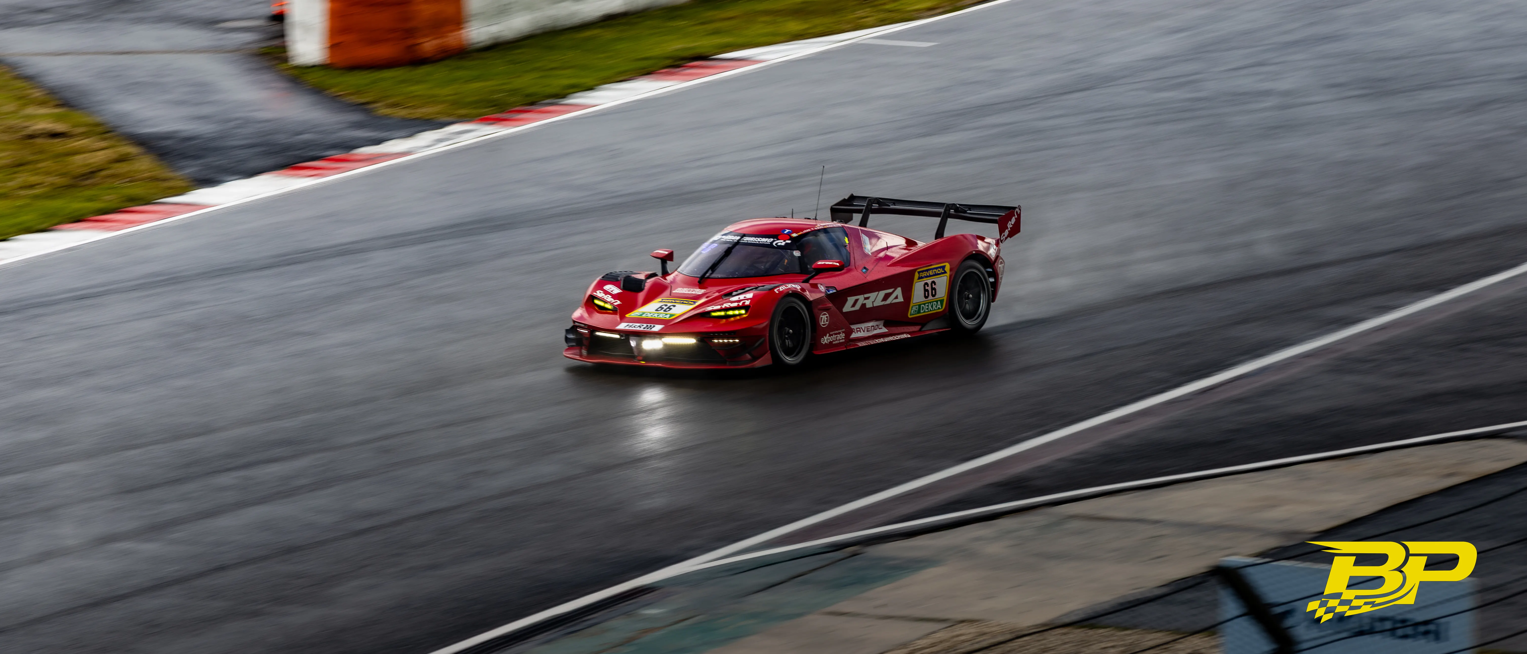 Red No. 66 race car cornering with headlights on over wet asphalt.