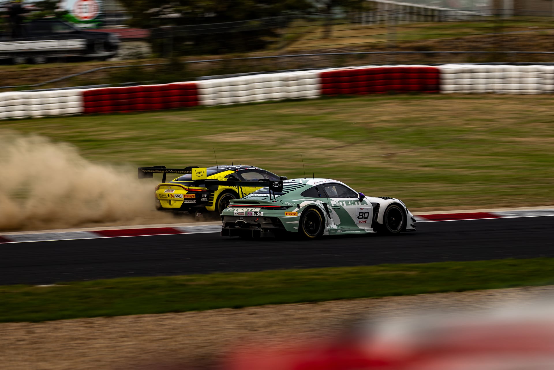 Two GT race cars battling through a corner on a racing circuit, showing close motorsport action and trackside atmosphere.