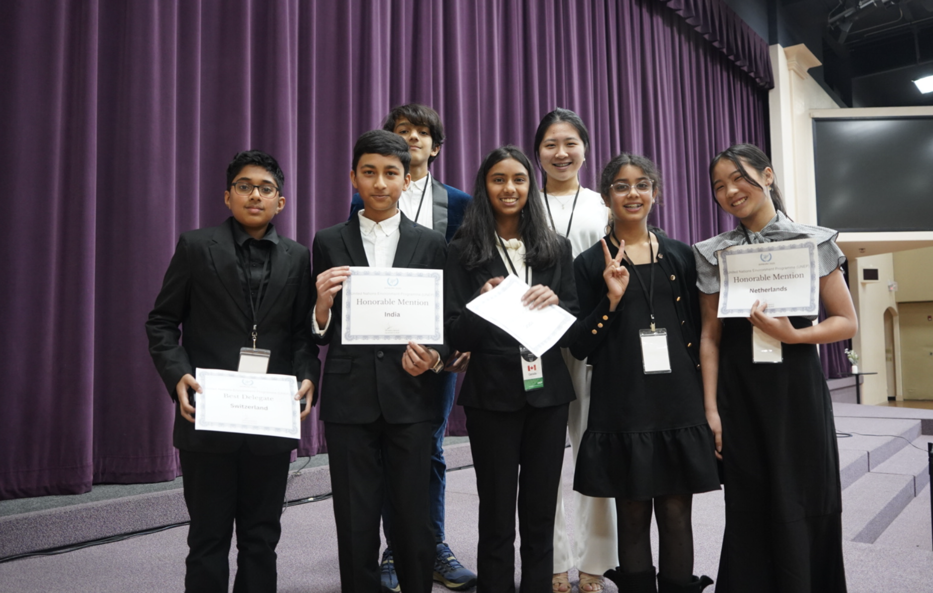 Group of students and adults holding certificates in front of a stage.