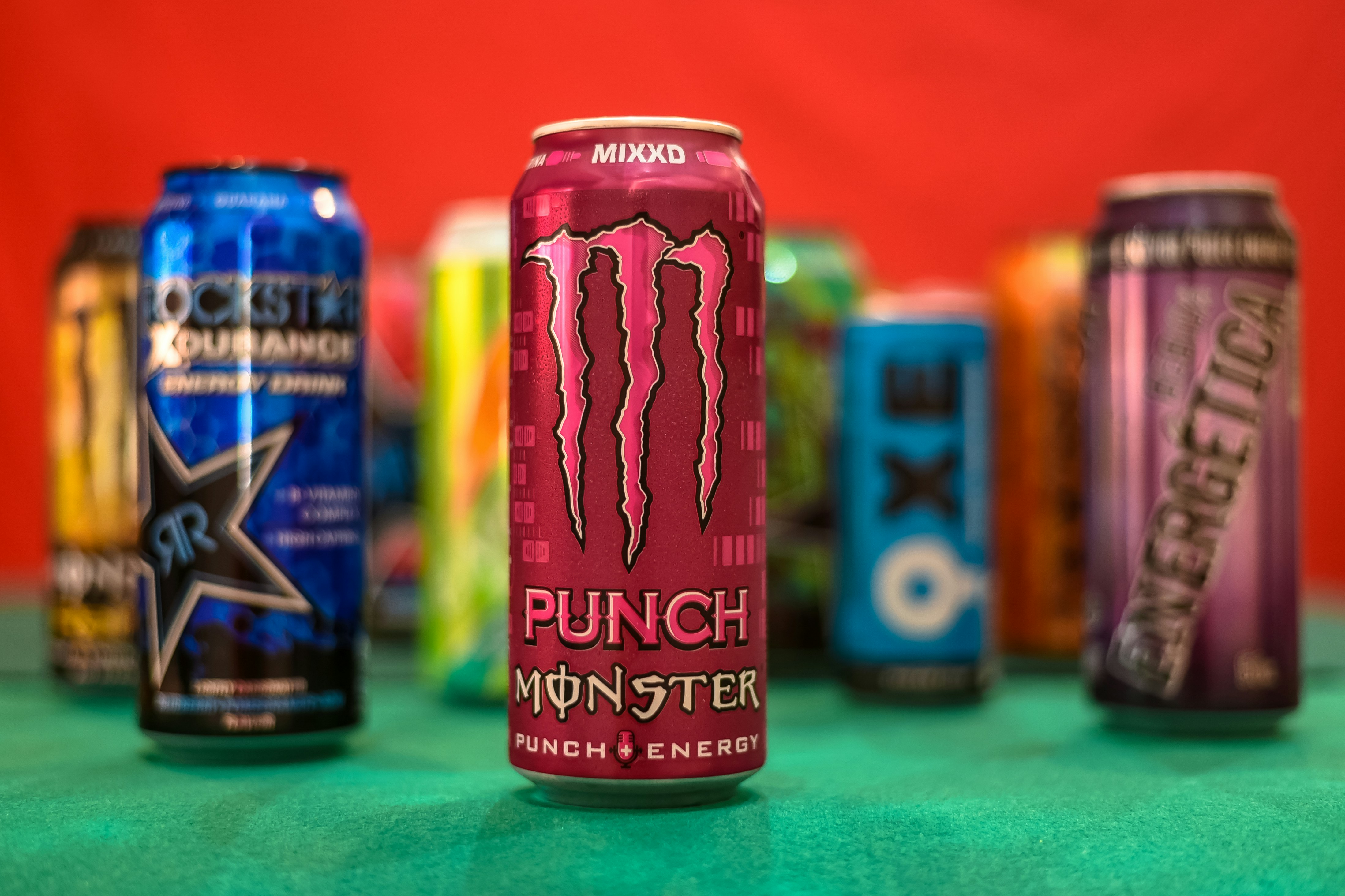 Several colorful energy drink cans arranged on a green surface against a red background.