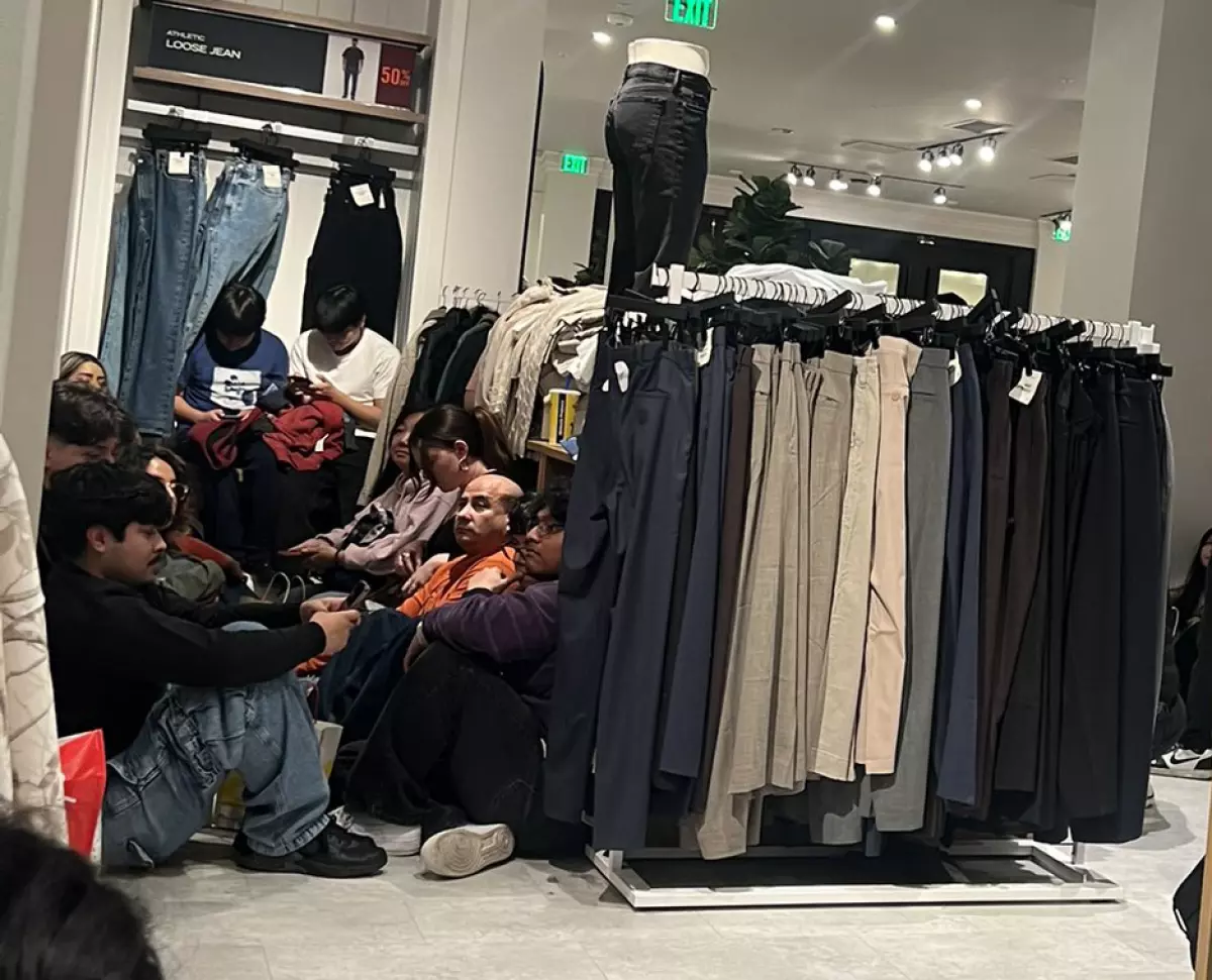 People sit on the floor among clothing racks inside a store.